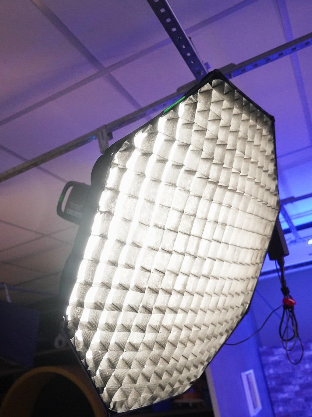 Softbox octogonal com colmeia, presa no trilho do teto, sob luz roxa.
